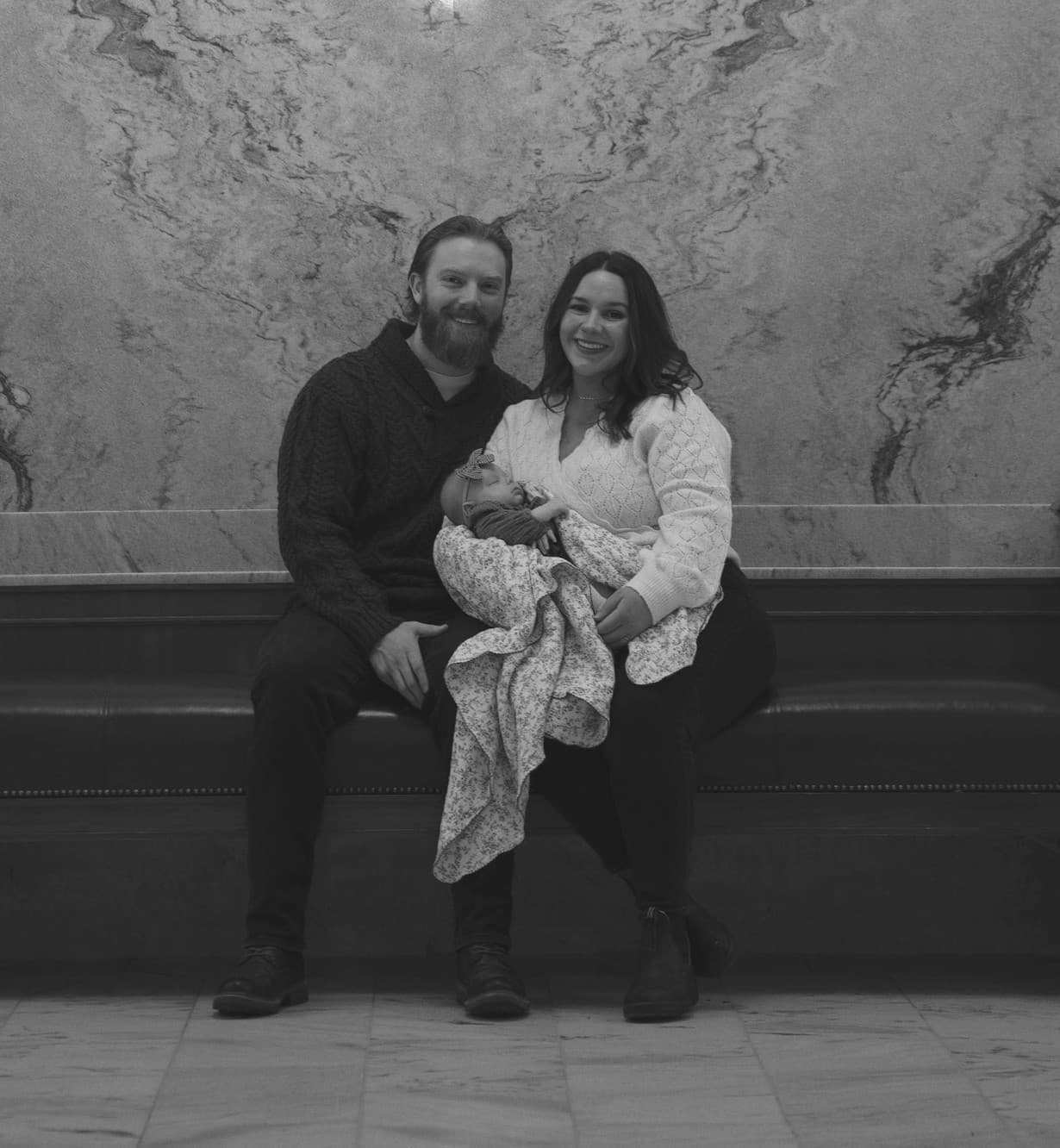 Jesse and his wife smiling on a bench, holding their baby daughter